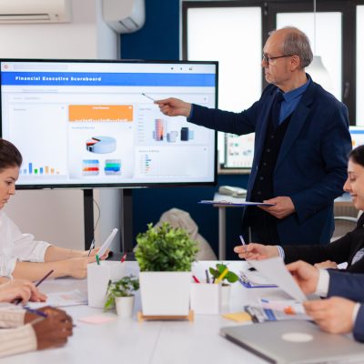 Senior team leader explaining presentation discussion in conference room briefing planning. Corporate staff discussing new business application with colleagues looking at screen